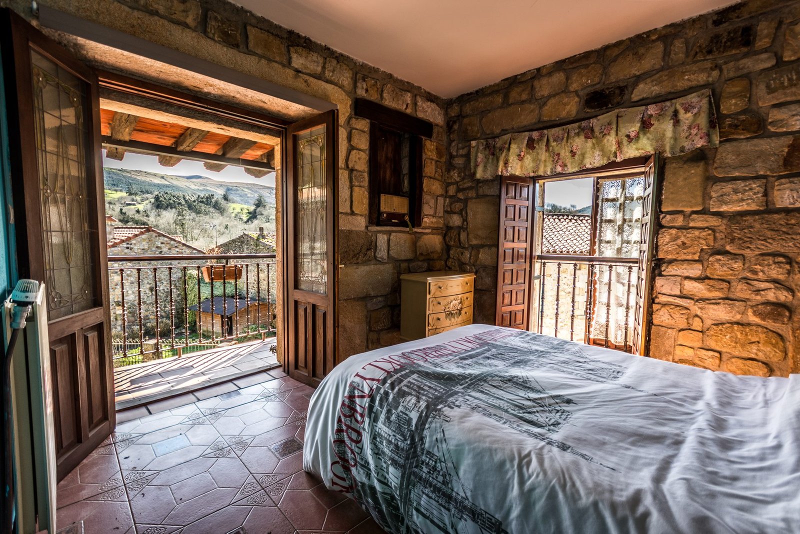Habitación con muros de piedra vista, balcón abierto a las montañas verdes de Cantabria